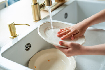 Closeup Little girl washes dishes with an eco-friendly brush made of natural materials near the sink. Child helps mother in the kitchen. Housework.