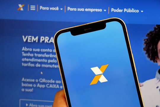 Bahia, Brazil - August 14, 2025: Caixa Econ&ocirc;mica Federal banking app on smartphone with website in the background. Brazilian bank. 