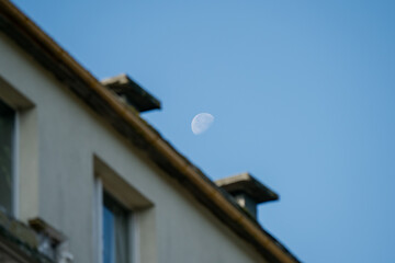 Half moon above old residential building rooftop symbolizing urban housing challenges, rising living costs, city life struggles and search for affordable homes