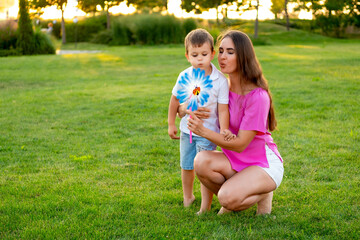 Fototapeta premium a mother and her child playing on a green lawn in the summer, having fun together, a mother and son walking together on a summer evening, playing a game, laughing and smiling