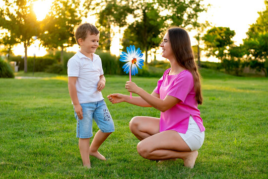 a mother and her child playing on a green lawn in the summer, having fun together, a mother and son walking together on a summer evening, playing a game, laughing and smiling - Powered by Adobe