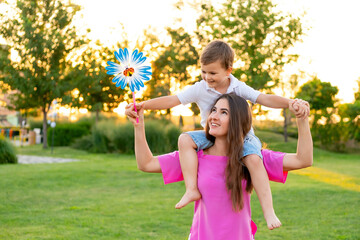 Obraz premium mom and baby playing on a green lawn in the summer, having fun together, mother and son walking together on a summer evening, with the baby on her neck