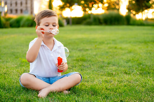 a little boy with bubbles is playing on a green lawn in the summer, having fun, a child is walking in the summer evening laughing and smiling, summer holidays