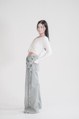 Pretty young fashion sensual woman posing on white wall background dressed in white top and jeans style outfit. Stylish fashionable girl in basic clothes