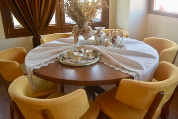 Dining table and chairs in elevated high end restaurant at a grape and olive farm in Crete Greece; decorated with white fabric linen, china plates and tea glasses, and faux dried flowers