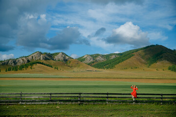 Caucasian woman in red dress enjoying scenic mountain landscape with green fields