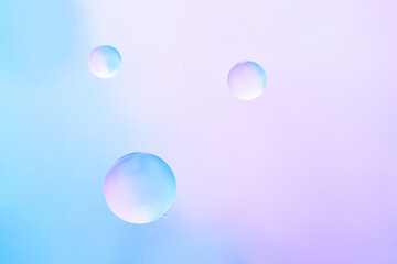 Minimal abstract composition with three transparent oil bubbles floating against a smooth gradient background in soft blue and lavender tones. Macro shot emphasizing clarity and simplicity