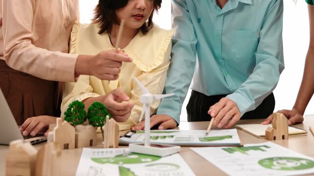 Business team consulting and analyzing green power graph usage for future esg of company. Windmill model represented using clean energy and house block symbolized eco house on the table. Delineation.