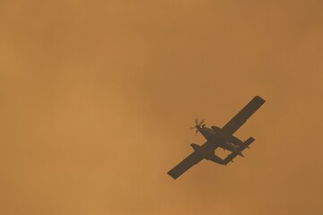 Firefighting airplane battling wildfires against a backdrop of a smoky, orange sky, showcasing the urgency of aerial rescue efforts