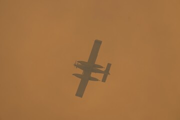 Fototapeta premium Powerful firefighting aircraft soaring above wildfire smoke, dropping water to combat intense forest blaze spreading across leon's rugged landscape in spain