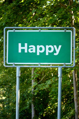 Fototapeta premium Green road sign with the word Happy against a background of leafy trees