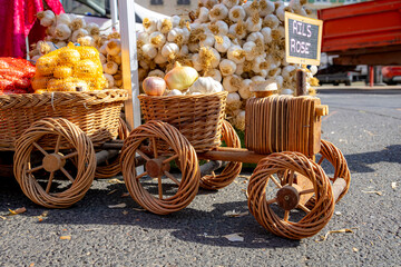 Decorative wicker cart filled with fresh garlic and onions at French farmers market. Traditional basket display with "Ails Rose" sign. Rustic market scene.