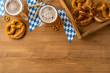 Oktoberfest celebration featuring cold beer mugs, salted pretzels, and Bavarian flag patterns on flatlay overhead view wood