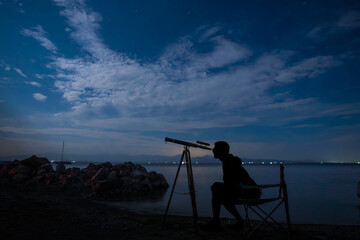 Silhouette of person looking in the telescope at the starry night.