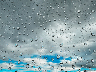 Raindrops on glass create a beautiful, atmospheric scene with a cloudy sky background. Close-up of raindrops on glass with a cloudy sky background, a beautiful and peaceful scene.