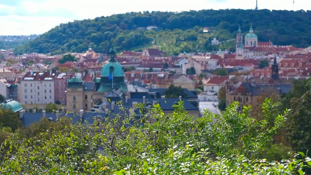 Prague cityscape with petrin hill and st. Nicholas church. Lush green leaves frame a picturesque view of prague, showcasing the cityscape with petrin hill and st. Nicholas church under a serene sky