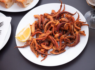 Fried spicy tentacles squid served on white plate with potatoes, lemon slices