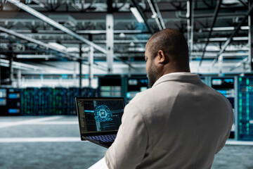 Admin using laptop in data center housing advanced equipment used for storing AI training datasets. Server room IT professional running artificial intelligence code to resolve technical issues