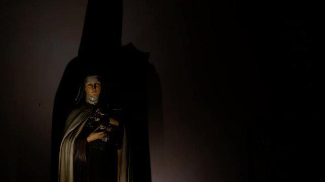 Saint therese of lisieux statue casting shadow on wall. Warm light illuminates a statue of saint therese of lisieux, also known as saint th&eacute;r&egrave;se of the child jesus and the holy face