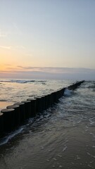 sunset on the beach Wooden breakwater stretching into the sea at sunset, with gentle waves and warm golden light.