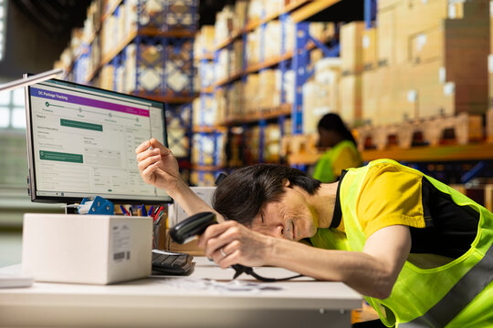 Tired employee deals with burnout and takes a nap with scanner in his hand, scanning shipping labels at warehouse desk. Order fulfillment and inventory management in a long shift.