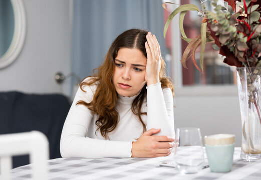 Depressed young woman sitting at table. Portrait of sad woman at home. - Powered by Adobe