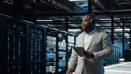 Data center admin wearing headphones using tablet to identify bottlenecks. Server farm IT expert...