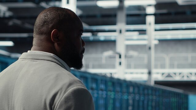 System administrator in data center doing inspection on infrastructure tech handling user requests. African american worker in server farm analyzing traffic patterns of equipment, camera B