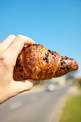 Fresh croissant displayed in hand under bright sunlight