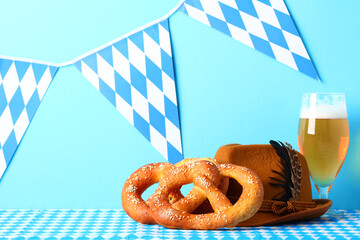 Oktoberfest celebration concept. Foamy beer, golden pretzels, and alpine hat on Bavarian tablecloth with festive bunting on bright blue background.