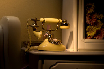 Landline. An old, antique corded telephone, illuminated at night, standing on a white sideboard. Traditional telecommunications. Telephone calls over a retro telephone.. Evening conversations