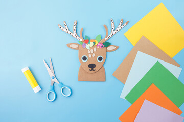 Cardboard reindeer head with colorful paper crown, craft tools, and sheets for holiday workshops, school art projects, creative hobby businesses, and handmade decoration product branding,