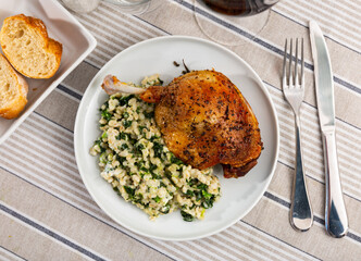 Czech cuisine. Fried duck leg with wheat porridge (perlovka) with spinach served on white plate