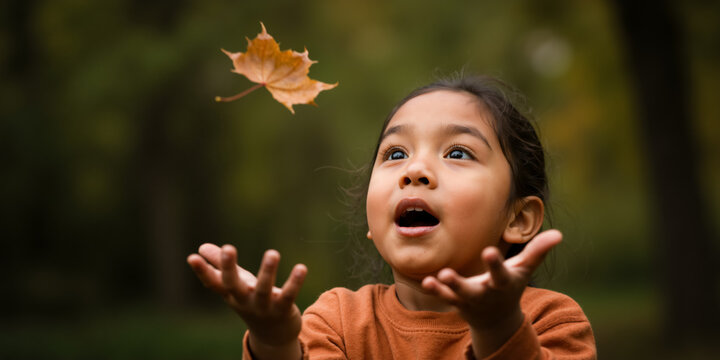 Girl with a look of wonder catching a falling autumn leaf. Child playing in a park in fall.