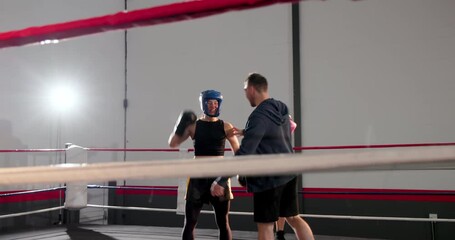 Trainer fixing rope in ring, fitting pads, guiding sparring for training, black boxer raising arms