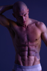 Fototapeta premium Muscular man striking a pose against a dramatic background. The lighting creates engaging shadows to emphasize his toned physique and strength.