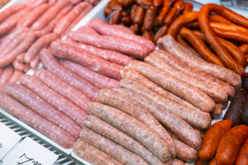 Raw pork-beef sausages in packing tray on glass window refrigerator of butcher shop. Fresh sausages ready for barbecue