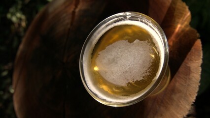 A small glass of beer on the table. A glass of beer on a wooden table. A beer glass outdoors