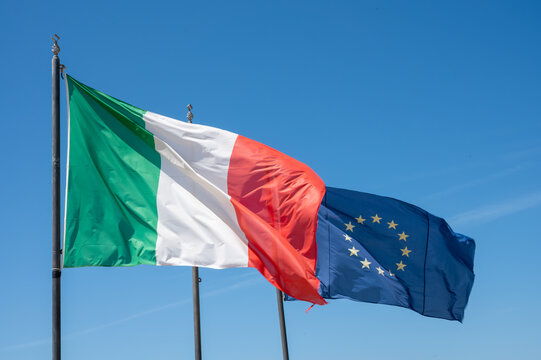 Green-white-red national italian flag and blue with stars flag of EU, waving on mast in sunny day in blue sky