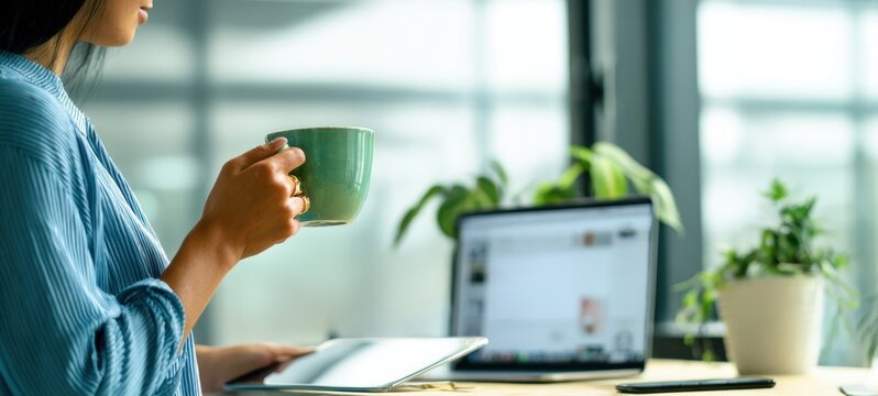 The person holding a green mug at a home office desk with laptop