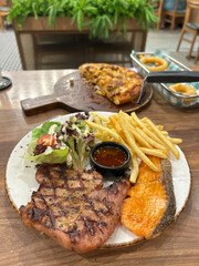 Grilled pork steak and a succulent salmon fillet, complemented by crispy fries, a fresh salad and a Thai savory dipping sauce in the restaurant