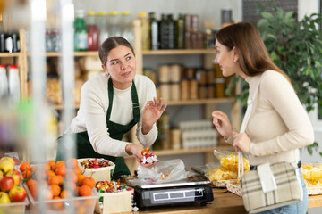 Helpful female vendor weighs candies on scales and sells candies to customer