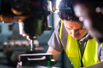 Skilled worker focused on operating machinery in a factory. Wearing high visibility vest and gloves, demonstrating precision, technical ability, safety, and industrial expertise.