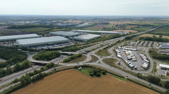 Aerial drone footage, busy motorway M1 and roundabout junction with industrial warehouses distribution centres and motorway services near Coventry England UK