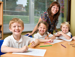 Teacher and happy children in class. A group of primary school pupils and their female teacher all smile happily at the camera during a lesson in a classroom. From a series of images.