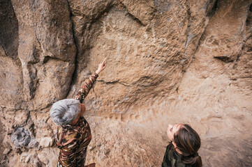 Fototapeta premium Mother and daughter dressed in hiking clothes, walking along a cliff observing cave paintings. 