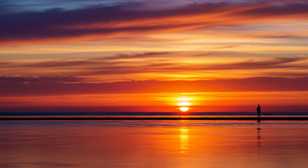 Obraz premium Vibrant Sunset Reflection with a Lone Figure on the Horizon