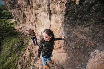 Obraz premium Mother and daughter on a hike through the countryside where they found cave paintings on a cliff, dressed in hiking clothes.