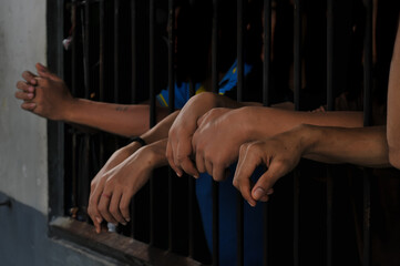 Close-up of an inmate&rsquo;s hand holding prison bars in a dark cell. Concept of imprisonment, punishment, confinement, and criminal justice.