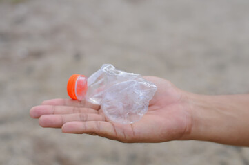 Close-up of a hand picking up a plastic drink bottle as waste. Concept of recycling, environmental protection, and waste management.